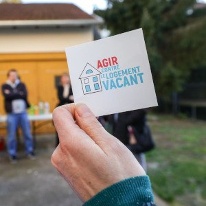 Une personne tient un sticker portant la mention "Agir contre le logement vacant".